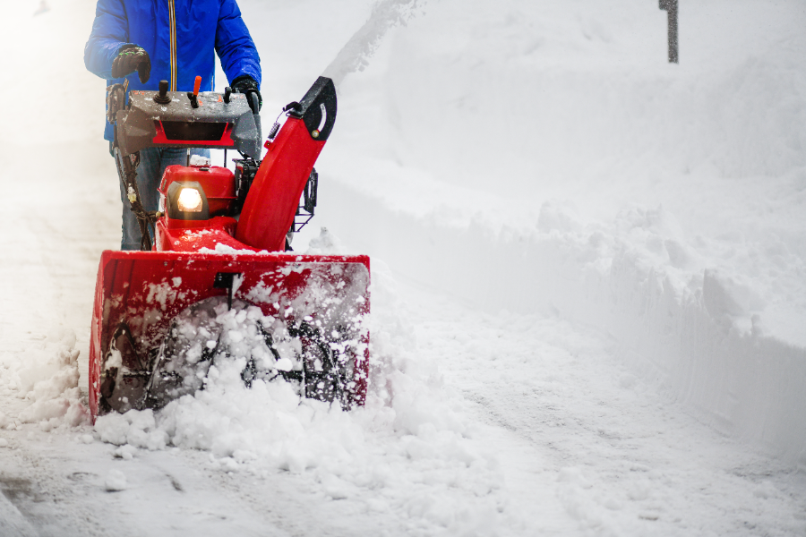 Person operating red snow blower on snow-covered residential street